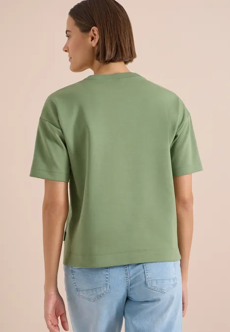 Person von hinten in grünem T-Shirt und blauen Jeans.